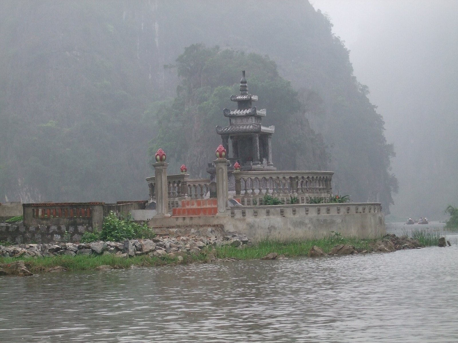 A small tiered stone pagoda on a walled bank by the river, with limestone hills in mist behind