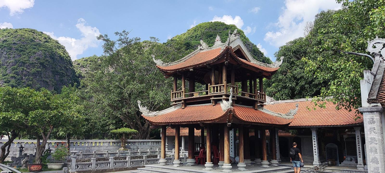 A two-storey bell tower with curved red-tiled roofs below green limestone hills at Thái Vi temple