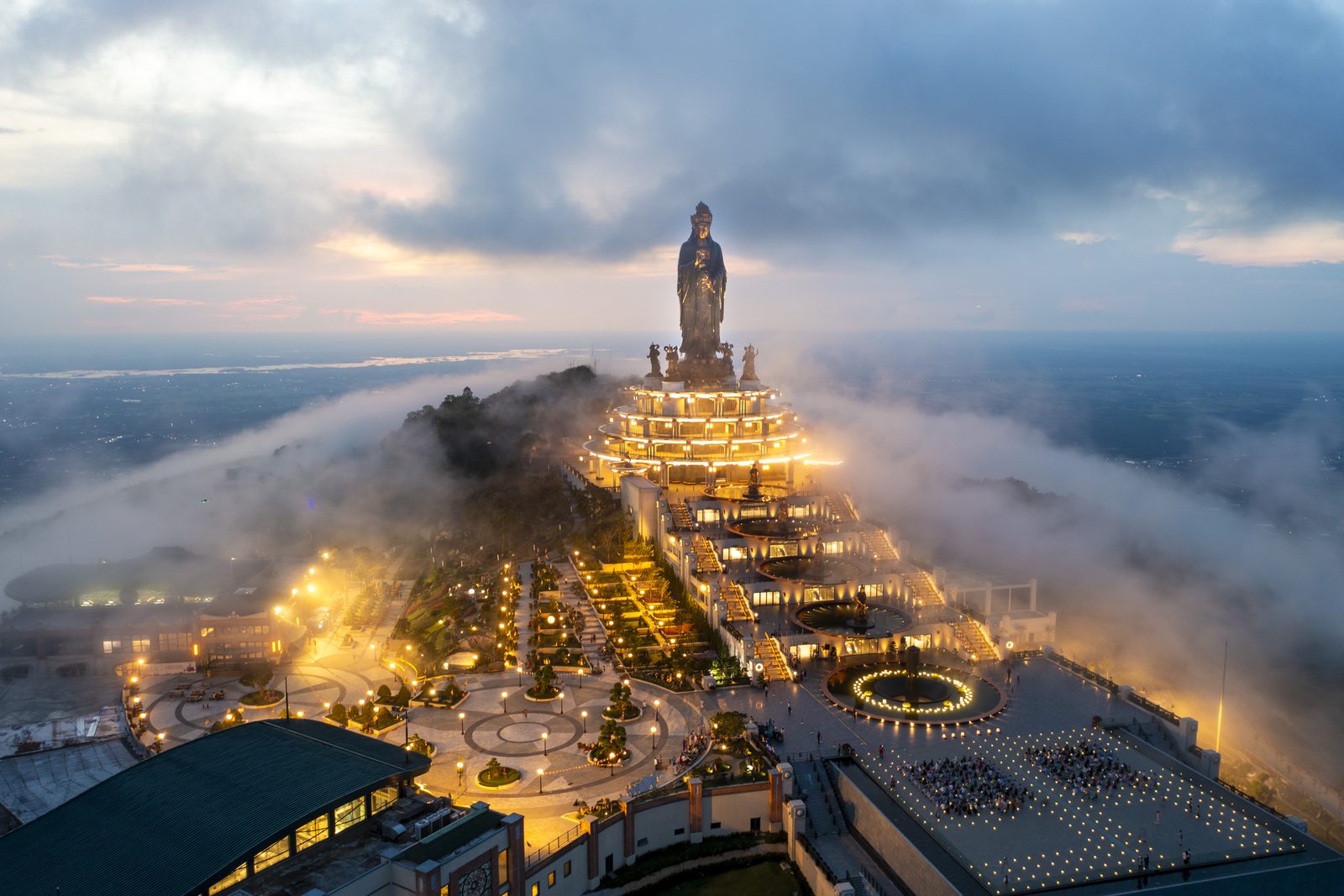 The illuminated Ba Den summit statue above a cloud layer at dusk
