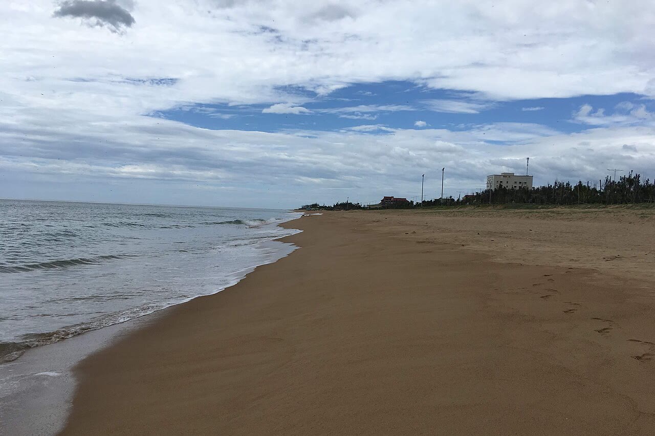 Surf and a wide sandy beach in Tuy Hoa, with casuarina and a building along the shore