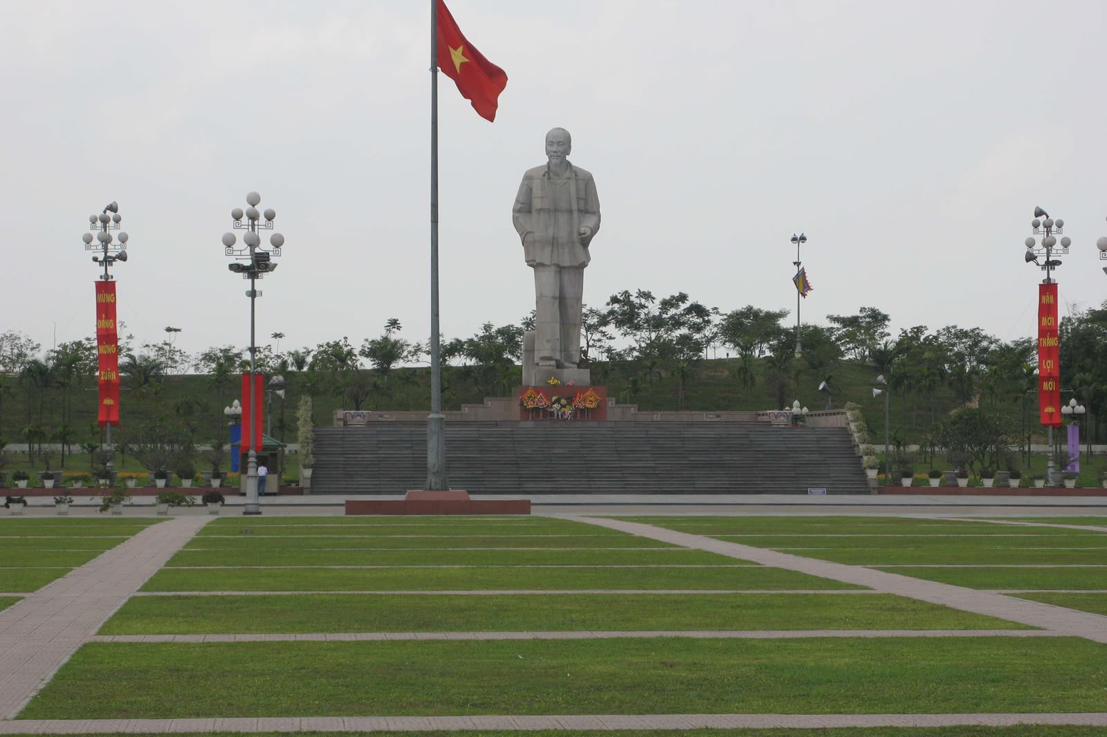The open lawn of Ho Chi Minh Square in Vinh, with the full statue and a Vietnamese flag